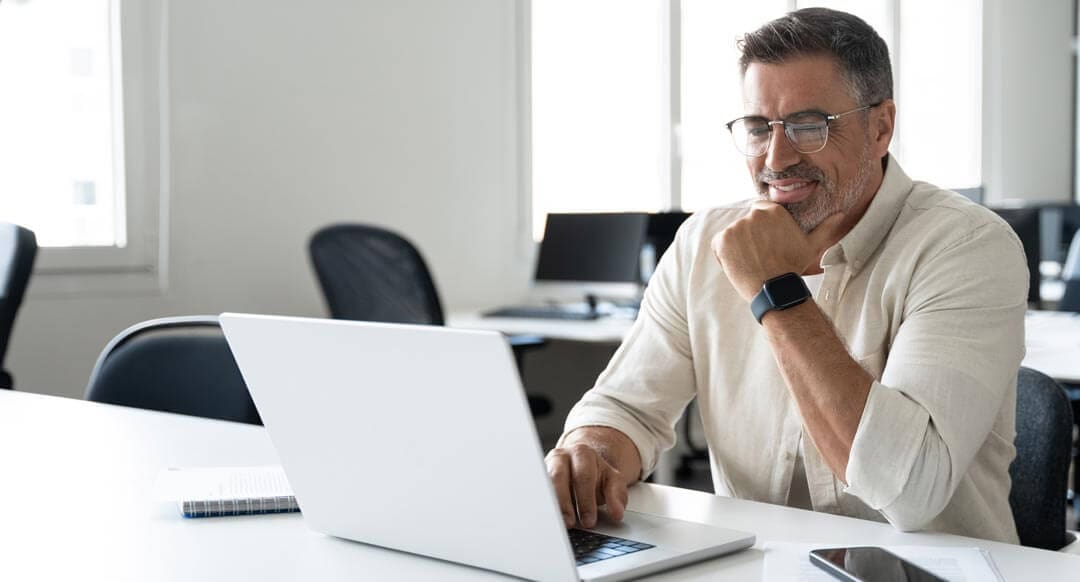 Businessman doing online data market analysis, thinking planning tech strategy at laptop. Happy smiling mature Indian or Latin business man ceo trader using computer, typing, working in modern office.